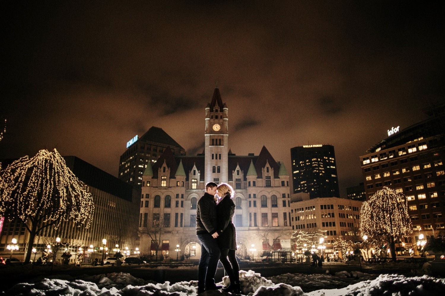 an engaged couple in close embrace in front of a beautiful city nightscape