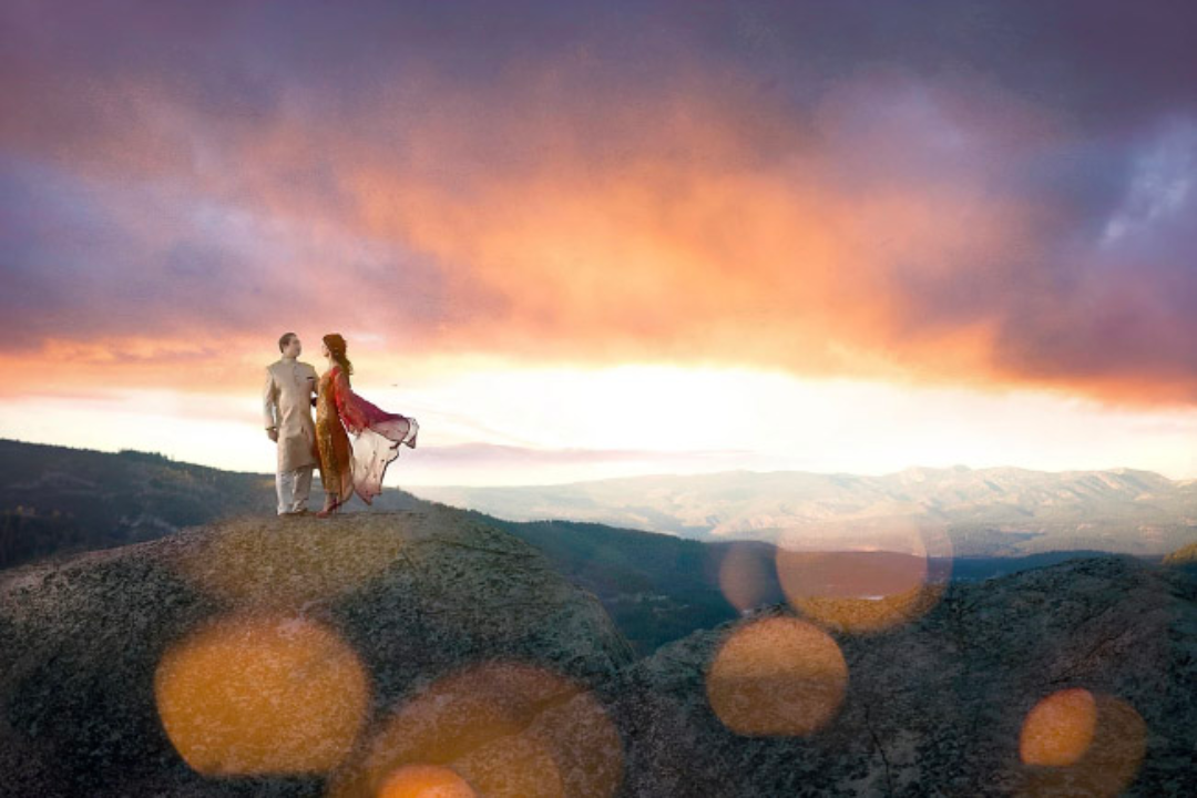 Bride and groom dressed in traditional Indian wedding clothes posing on top of a cliff