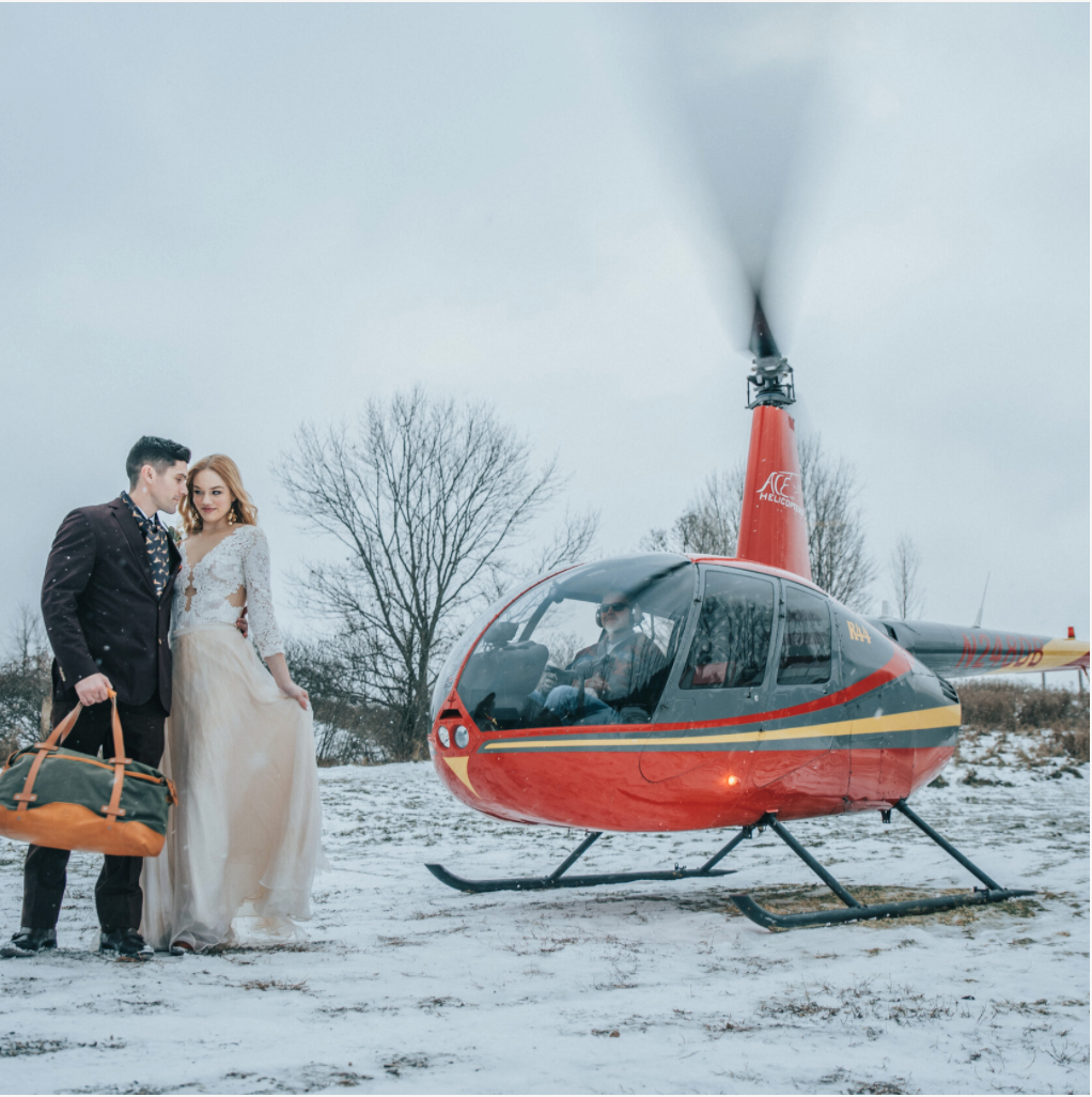 A bride and groom posing in front of a helicopter