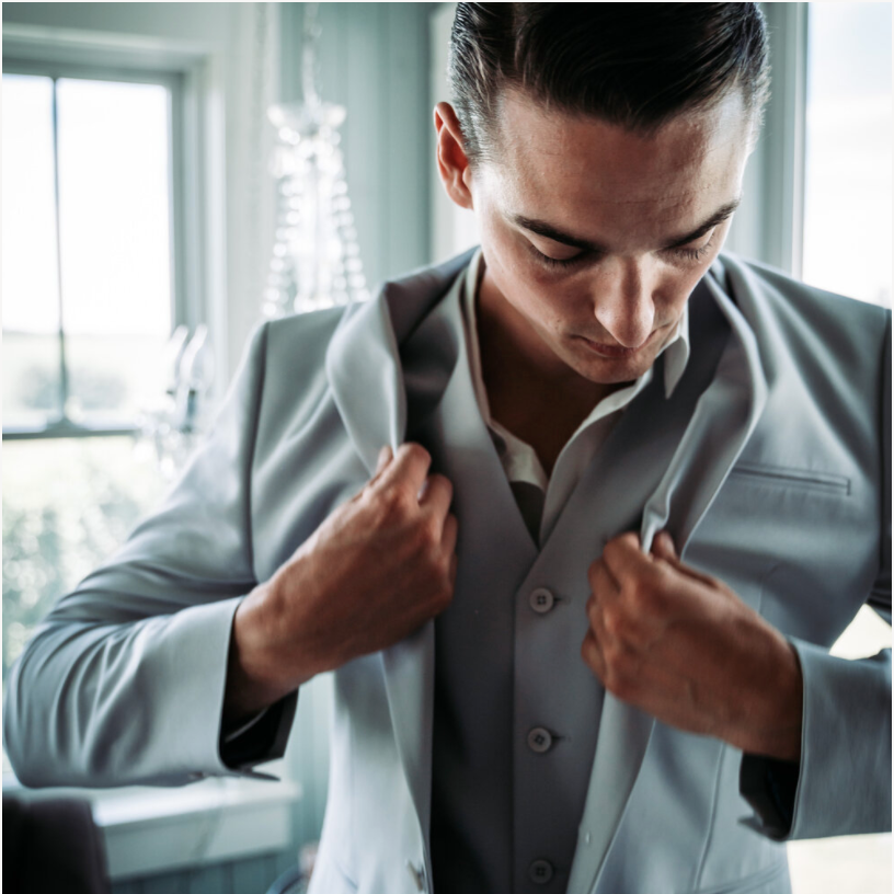 A groom to be getting ready wearing his tuxedo jacket